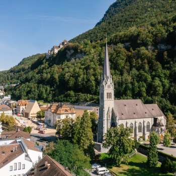 Aerial view of St. Florin's Cathedral in Vaduz with Vaduz Castle in the background on a sunny day.