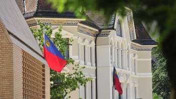 View of the façade of the government building in Vaduz with Liechtenstein flags flying in the foreground.