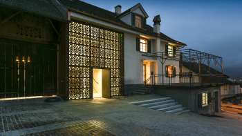 Modern illuminated Kulturhaus Rössle in Mauren at dusk, with glass façade, historic building extension and paved forecourt.