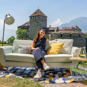 Woman sitting on a sofa with a view of Vaduz Castle and the mountains of Liechtenstein, modern outdoor ambience with decoration