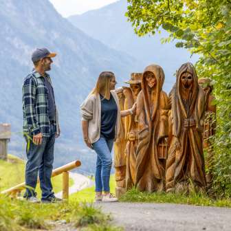 Couple looking at carved wooden figures on the Walser Legend Trail in Triesenberg with a view of the valley and mountains in the background