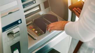 Woman entering a PIN while holding a wallet at a generic ATM