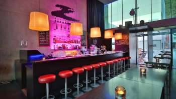 Modern bar with a long counter, red bar stools, and stylish lighting