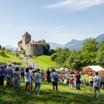 Visitors gather for the 2024 State Act in Liechtenstein on the meadow below Vaduz Castle