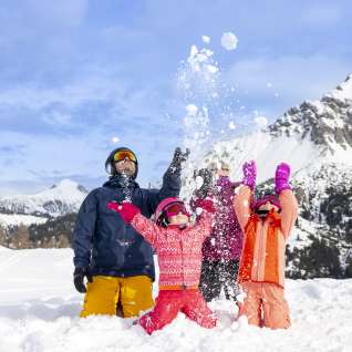 Family enjoying the snow together in Malbun - children happily throwing snowballs against a wintry mountain backdrop.