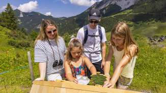 Family explores an interactive station on the themed trail in Malbun, surrounded by alpine scenery and summer meadows in Liechtenstein.