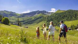 A family walks through a blooming summer meadow in Malbun, Liechtenstein, and enjoys the view of the surrounding Alps.