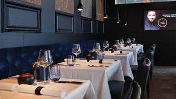 Elegant interior of the Esquire Bar & Bistro in Vaduz with stylishly laid tables, dark blue upholstered bench and atmospheric lighting.