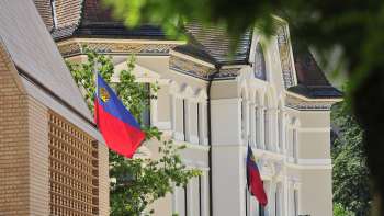 View of the façade of the government building in Vaduz with Liechtenstein flags flying in the foreground.