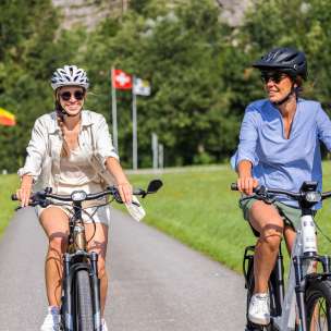 Two women on e-bikes on a summer tour with the flags of Liechtenstein, Switzerland and Austria in the background