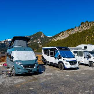 Several campers and motorhomes on a pitch in the mountains of Liechtenstein under a bright blue sky