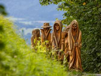 Detailed view of carved wooden figures in mystical depiction on the Walser Legend Trail in Triesenberg, surrounded by green nature