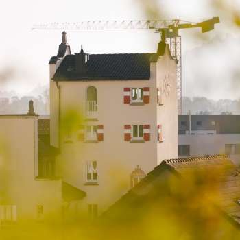 Close-up of the historic tower of Vaduz Town Hall with striking red shutters, surrounded by construction site cranes in the background.