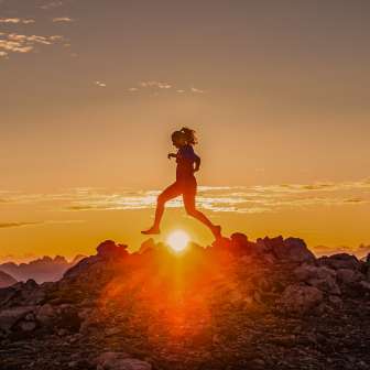 Two trail runners cross a rocky mountain ridge at sunrise in Liechtenstein, in the golden light of dawn