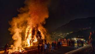 Large bonfire in Liechtenstein at night, people watch the blazing fire on a hill with a view of the illuminated city and the mountains.