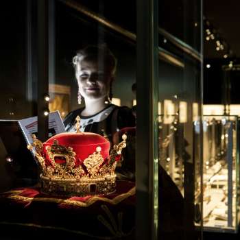 Woman looking at the princely hat in the Liechtenstein TreasureChamber, surrounded by illuminated display cases.