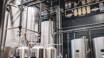 View of the brewery's technical room with its complex piping system and modern stainless steel tanks.