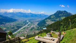Viewing platform with wooden fountain and view of the Rhine Valley and the Liechtenstein municipalities on a clear summer's day.