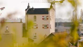 Close-up of the historic tower of Vaduz Town Hall with striking red shutters, surrounded by construction site cranes in the background.