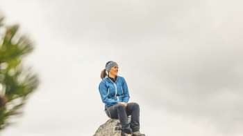 Rosaria Michaela Ackermannsits on a rock in the mountains of Liechtenstein and gazes into the distance