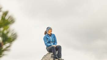 Rosaria Michaela Ackermannsits on a rock in the mountains of Liechtenstein and gazes into the distance