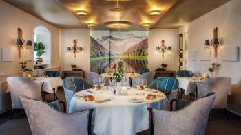 An elegant dining room with stylishly set tables, a sophisticated atmosphere, and a large landscape painting