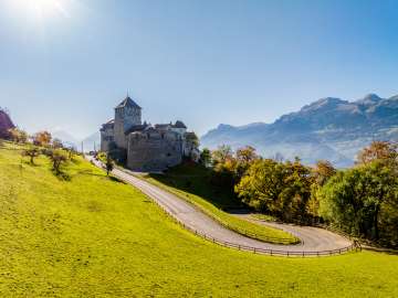 View of Vaduz Castle in Liechtenstein with autumnal trees and bright sunshine