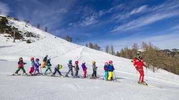 Ski instructor at Malbi Park Malbun motivates children on the practice slope - perfect environment for their first turns in the snow
