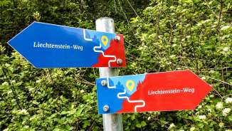 Colorful signpost of the Liechtenstein Trail with red and blue arrows against a green forest background