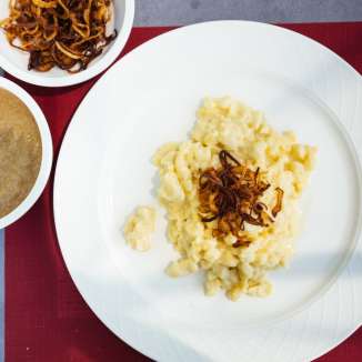 Traditional "Käsknöpfle" (cheese dumplings) with fried onions and apple sauce from Liechtenstein on a white plate