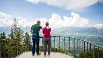 Two people enjoy the view from the Gaflei vantage point over the Rhine Valley in Liechtenstein on a clear day.