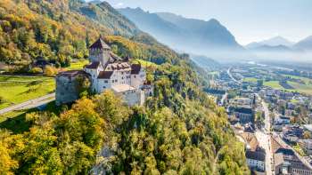 View of Vaduz Castle with autumn-colored forest and the town of Vaduz in the valley. View of Vaduz Castle with autumn-colored forest and the town of Vaduz in the valley.