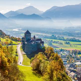 View of Vaduz Castle in Liechtenstein with an autumnal landscape and the Rhine Valley in the background