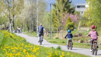 Family cycling on the spring cycle path in the Haberfeld Nature Park, surrounded by flowering meadows and trees.