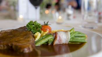 Close-up of a main course with green vegetables, bacon and creamy sauce on the plate