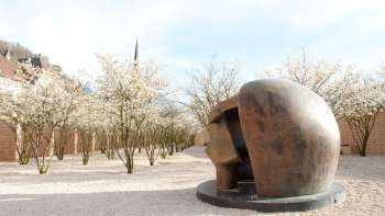 Bronze sculpture "Figure in a Shelter" by Henry Moore in the Vaduz Sculpture Park - surrounded by blossoming trees in spring.
