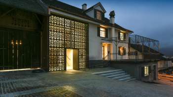 Modern illuminated Kulturhaus Rössle in Mauren at dusk, with glass façade, historic building extension and paved forecourt.