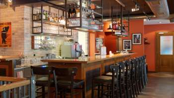 orne bar in the New Castle Vaduz with a long wooden counter, high chairs and hanging glass shelves in a warm ambience.