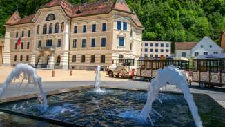 View of the government building in Vaduz with the Citytrain passing by and water fountains in the foreground