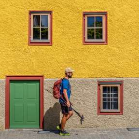 Hikers in front of the Landweibel-Huus in Schaan with its yellow façade, green door and red window frames - a highlight on the Liechtenstein Trail.