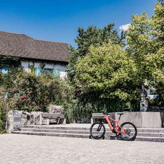 Red e-bike in front of a historic building in Liechtenstein, surrounded by trees and fountains, ideal starting point for a bike tour through the country