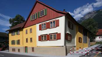 Traditional Landweibels-Huus with a yellow and red façade against a mountain backdrop in Liechtenstein.