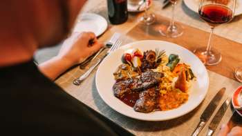 Close-up of a main course with meat, vegetables and fine sauces, accompanied by red wine