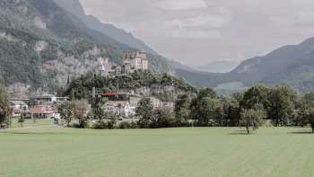 Majestic view of Gutenberg Castle in Balzers, surrounded by green fields and the impressive Alps.
