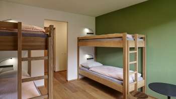 Four-bed room with bunk beds and hardwood floors at the Schaan-Vaduz Youth Hostel
