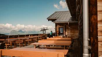 Empty wooden benches on the panoramic terrace of the Sareis hut with a view of the Alps - ideal for a break during a hike or ride on the mountain railroad.