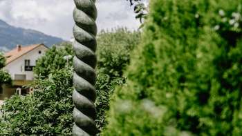 Renaissance artwork by Daniel Spoerri with striking column shape and bronze figure, surrounded by nature in Liechtenstein.
