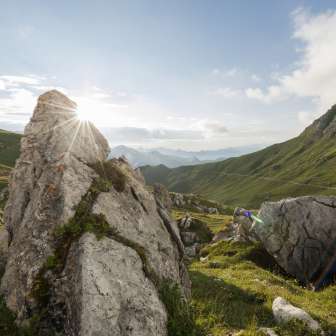Sunrise behind rock formations in the green Naaftal valley in Liechtenstein, surrounded by rolling hills and mountain scenery