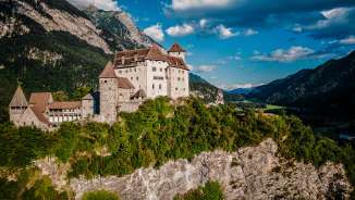 The imposing Gutenberg Castle is enthroned on a rock in Balzers, surrounded by green slopes and a majestic Alpine backdrop under a blue sky