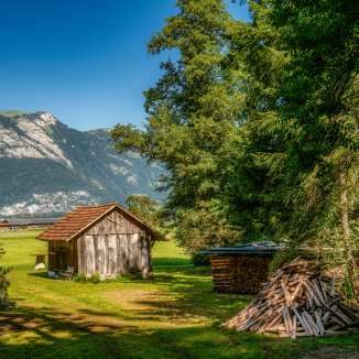 Small wooden barn on a meadow with a pile of firewood and a view of the Alps along Route 66 in Liechtenstein